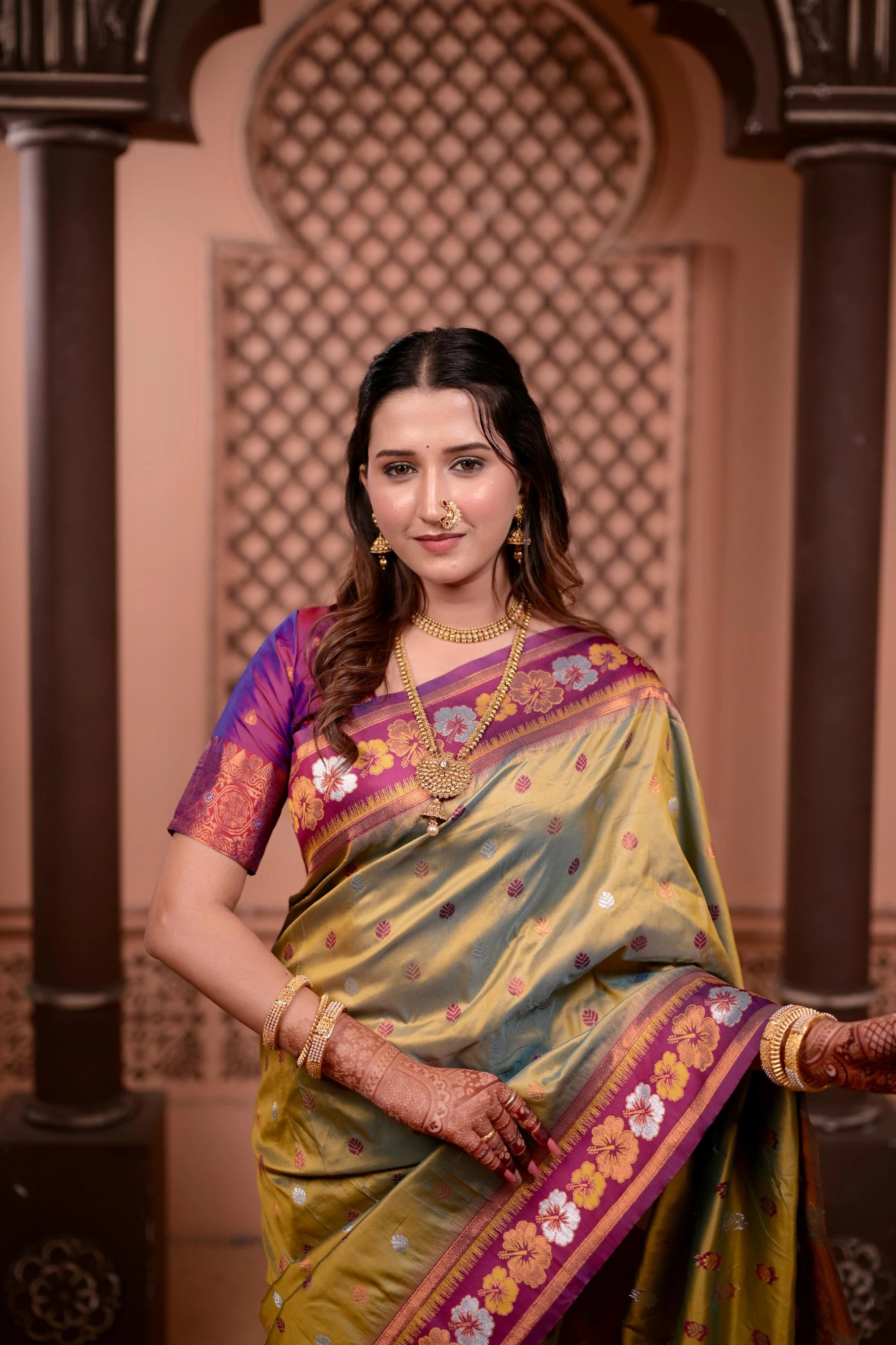 Woman in a traditional saree with intricate patterns against a decorative wall.